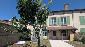 A house with a paved driveway, a small garden with a bench, and a tree.