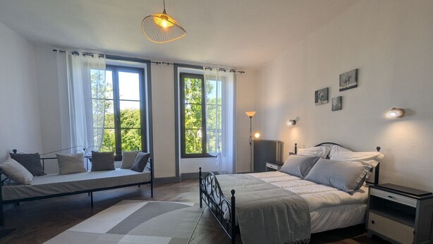A bedroom with a bed, a daybed, a floor lamp, and a wall-mounted light fixture.