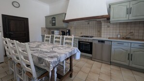A kitchen with a dining table, chairs, cabinets, a stove, and a clock on the wall.