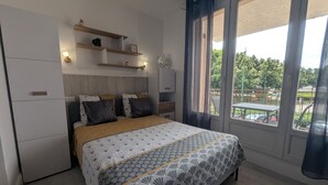 Un dormitorio con cama, mesitas de noche, armario, ventana con cortinas y vistas al exterior.