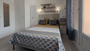 Un dormitorio con cama, mesitas de noche, armario y ventana con cortinas.