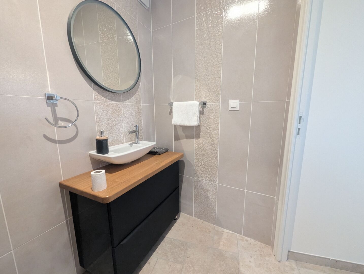A bathroom with a sink, mirror, towel rack, and a toilet paper roll on the counter.