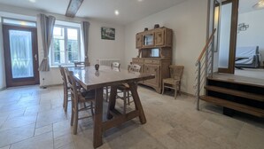 En rummelig spiseområde med et træbord og stole, et køkkenområde med skabe, og en trappe, der fører op til en etage.