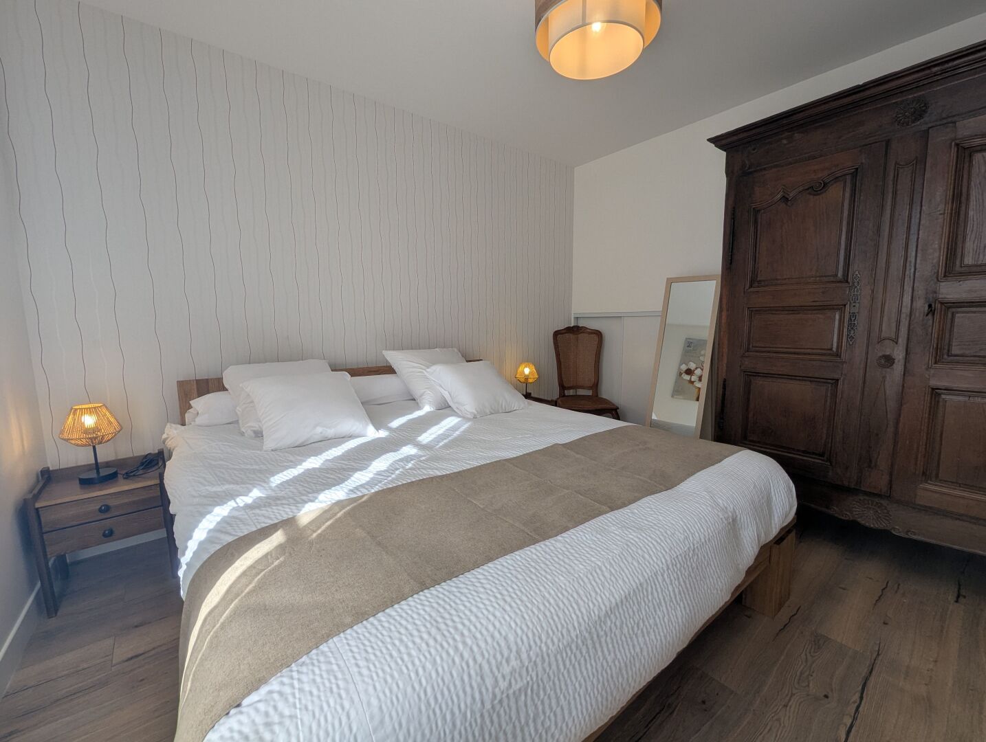 Een net opgemaakt bed met witte lakens, een houten hoofdbord en een grote kledingkast.