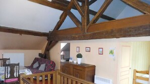 Une pièce chaleureuse avec un plafond en pente, des poutres en bois, un lit, un bureau, une chaise, un radiateur et une porte.