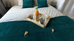 Un letto rifatto con una coperta verde, due cuscini e un vassoio con una bottiglia e dei bicchieri.