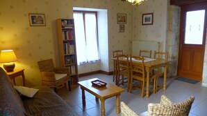 Een gezellige woonkamer met een bank, een houten tafel, een boekenkast en een eettafel met stoelen.