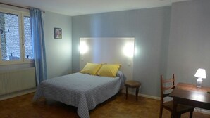 Een slaapkamer met een bed, nachtkastje, stoel, tafel en een raam met gordijnen.