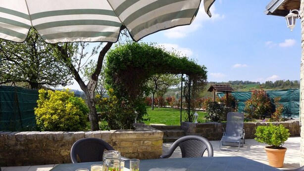 Patio esterno con tavolo apparecchiato per due, sotto ombrelloni a righe, circondato da muri in pietra e piante in vaso.