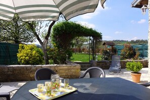 Eine Terrasse im Freien mit einem Tisch für zwei Personen, unter gestreiften Sonnenschirmen, umgeben von Steinmauern und Topfpflanzen.