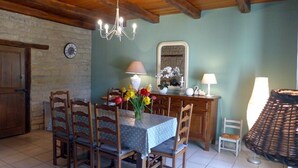 Zona pranzo con tavolo e sedie in legno, un lampadario e un vaso di fiori.