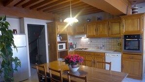 A kitchen with wooden cabinets, a white refrigerator, a microwave, an oven, and a dining table with chairs. - The White Stones (Aubepierre-sur-Aube)