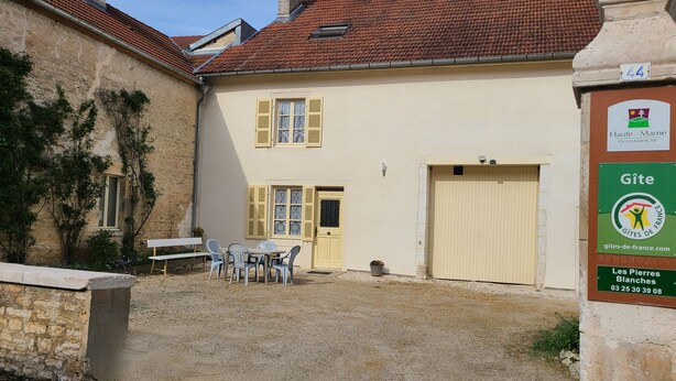 A building with a tiled roof, a door, and a window with shutters. There is a sign with a logo and text on the right side. - The White Stones (Aubepierre-sur-Aube)