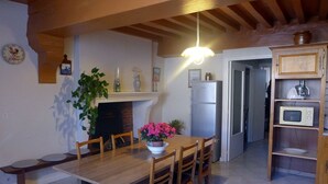 A dining area with a wooden table and chairs, a white refrigerator, a microwave, and a wooden cabinet with shelves. - The White Stones (Aubepierre-sur-Aube)
