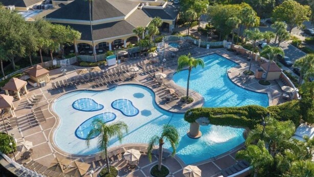 Un complexe hôtelier doté d’une grande piscine centrale, de plusieurs piscines plus petites et d’un espace extérieur bien entretenu, agrémenté de palmiers et de chaises longues.