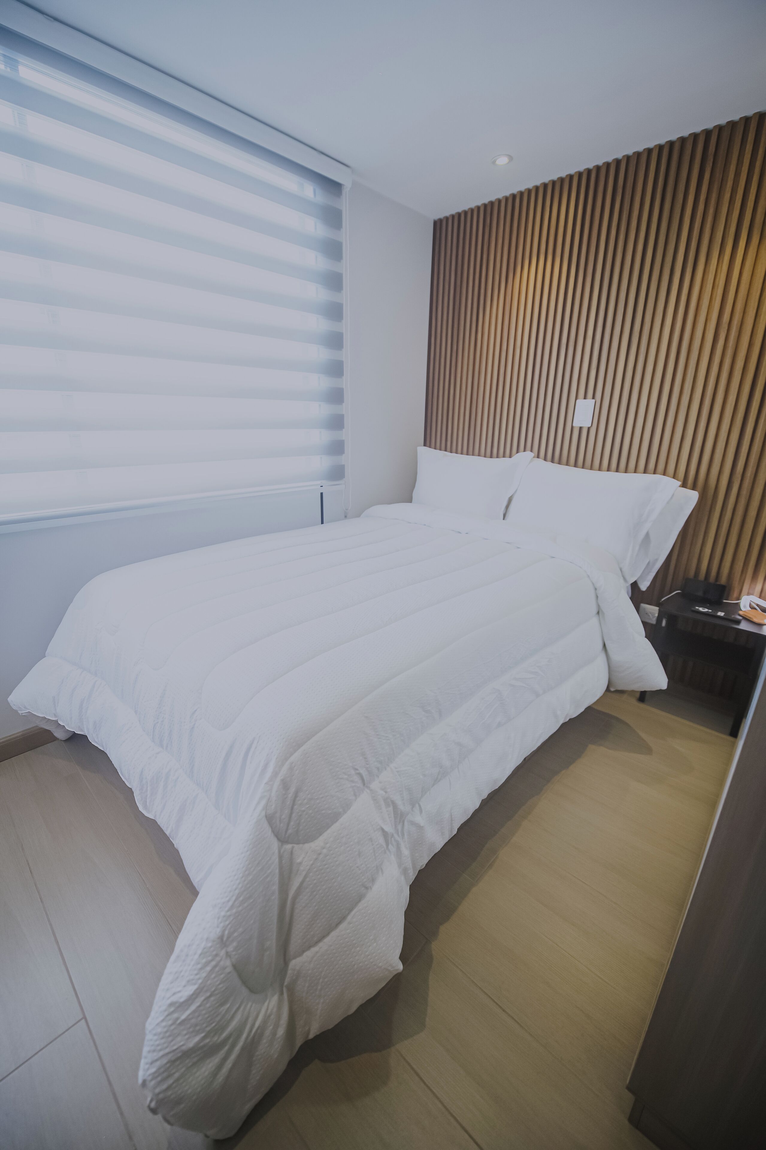 Une chambre d’hôtel moderne avec un grand lit, un mur lambrissé en bois et une table de chevet avec une lampe.