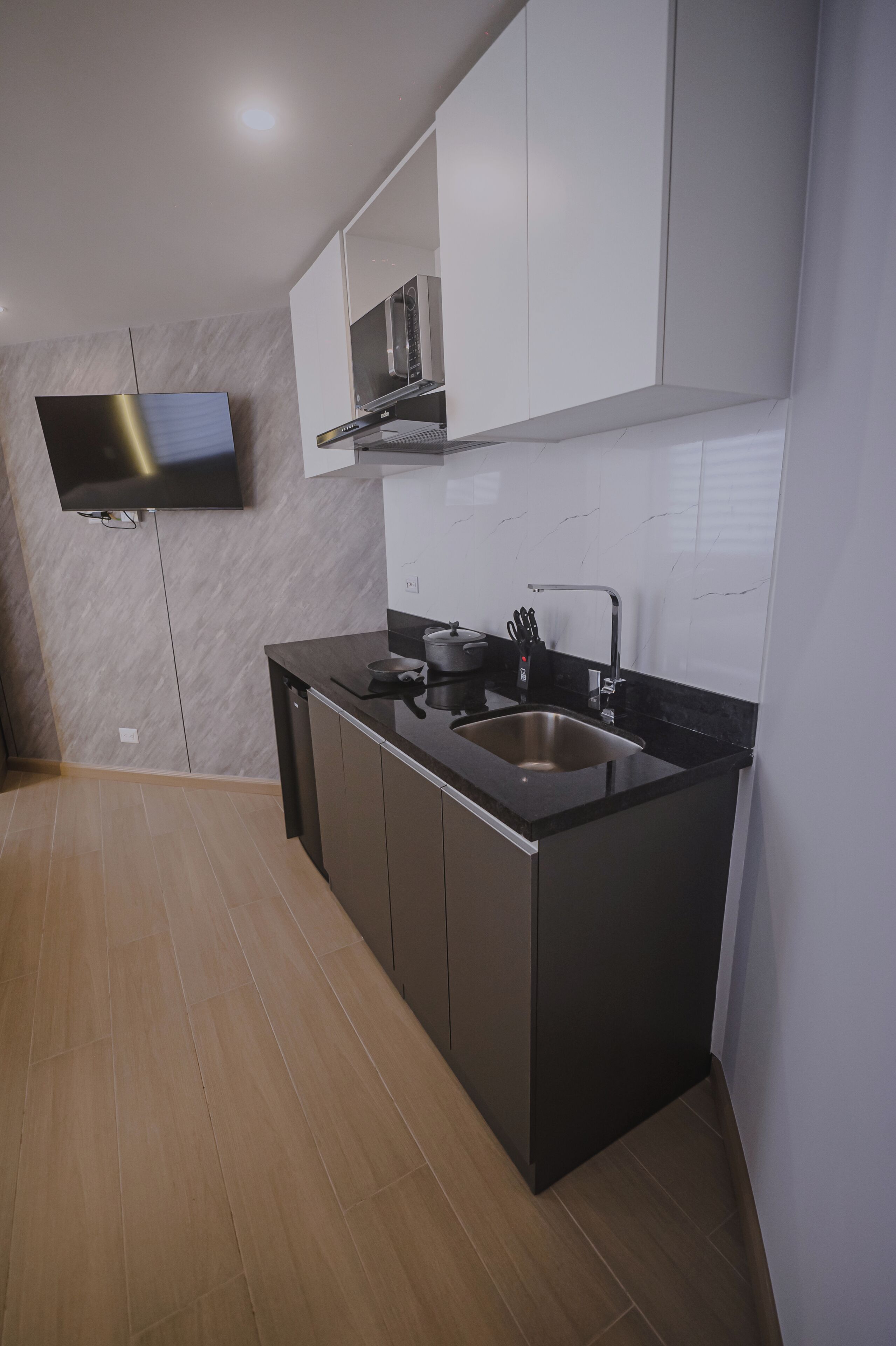 A modern kitchen with a black countertop, stainless steel sink, and a flat-screen TV mounted on the wall.