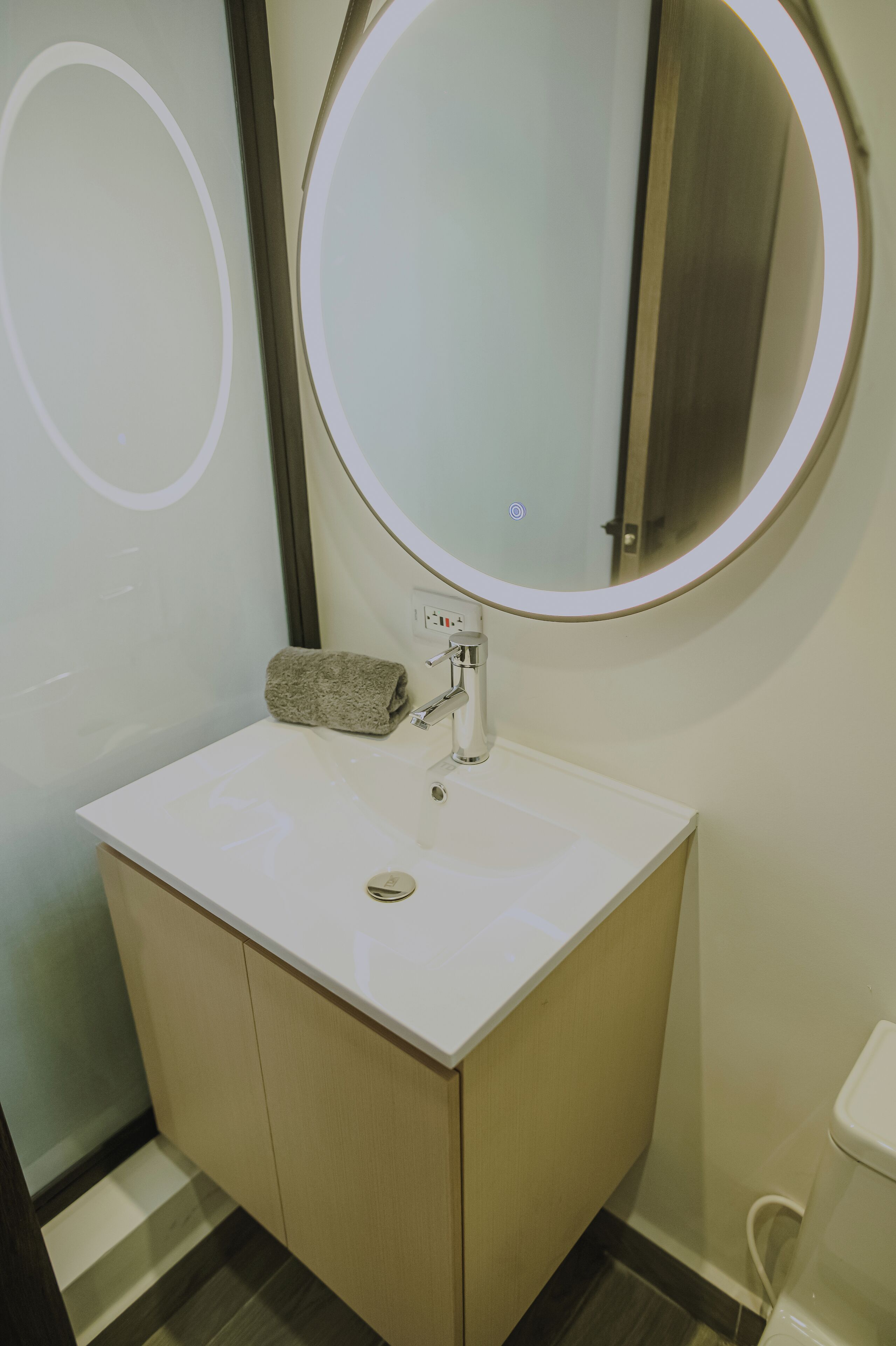A bathroom with a white sink, a round mirror, and a towel on the counter.