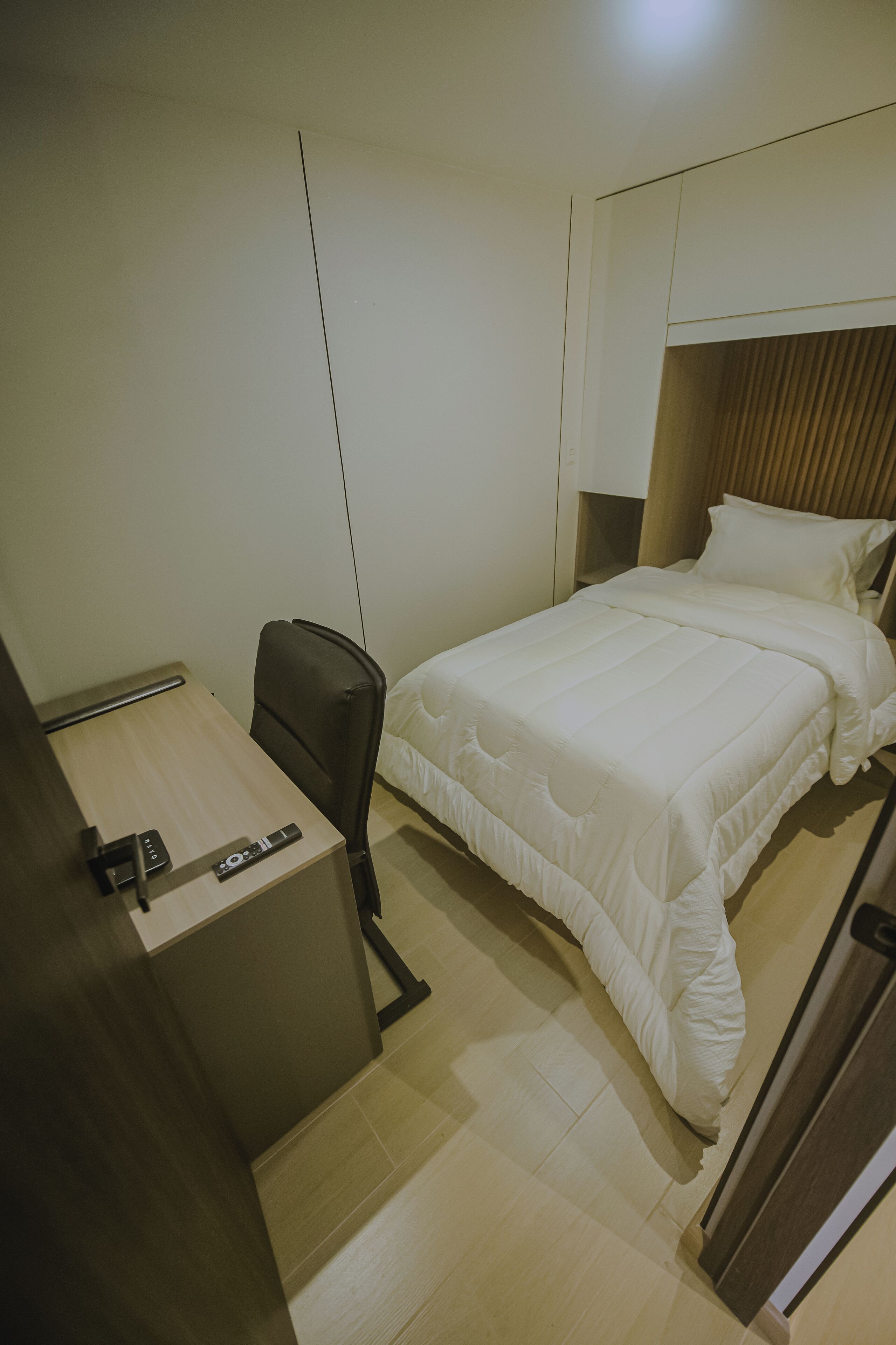 Une chambre d’hôtel de taille réduite, comprenant un lit simple, un bureau avec une chaise et une petite table.