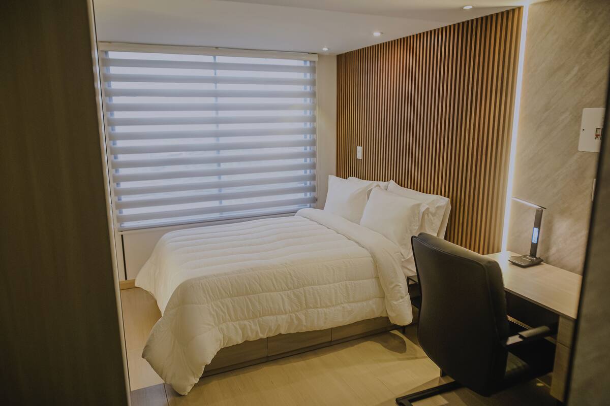 Une chambre d’hôtel moderne, équipée d’un lit, d’un bureau et d’une lampe.
