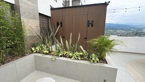 A rooftop garden with various plants, a wooden fence, and a view of the cityscape. - Torre U Kooliving (Manizales)