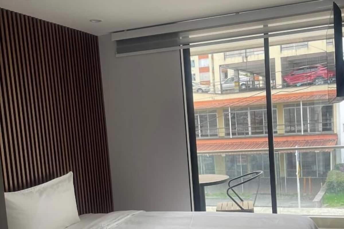 Une chambre moderne avec un grand lit, un mur recouvert de panneaux en bois et une vue sur un immeuble par une grande fenêtre.