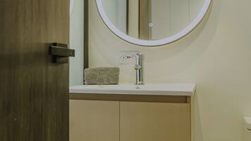 A bathroom with a wooden door, a white sink with a towel, and a round mirror with a light.