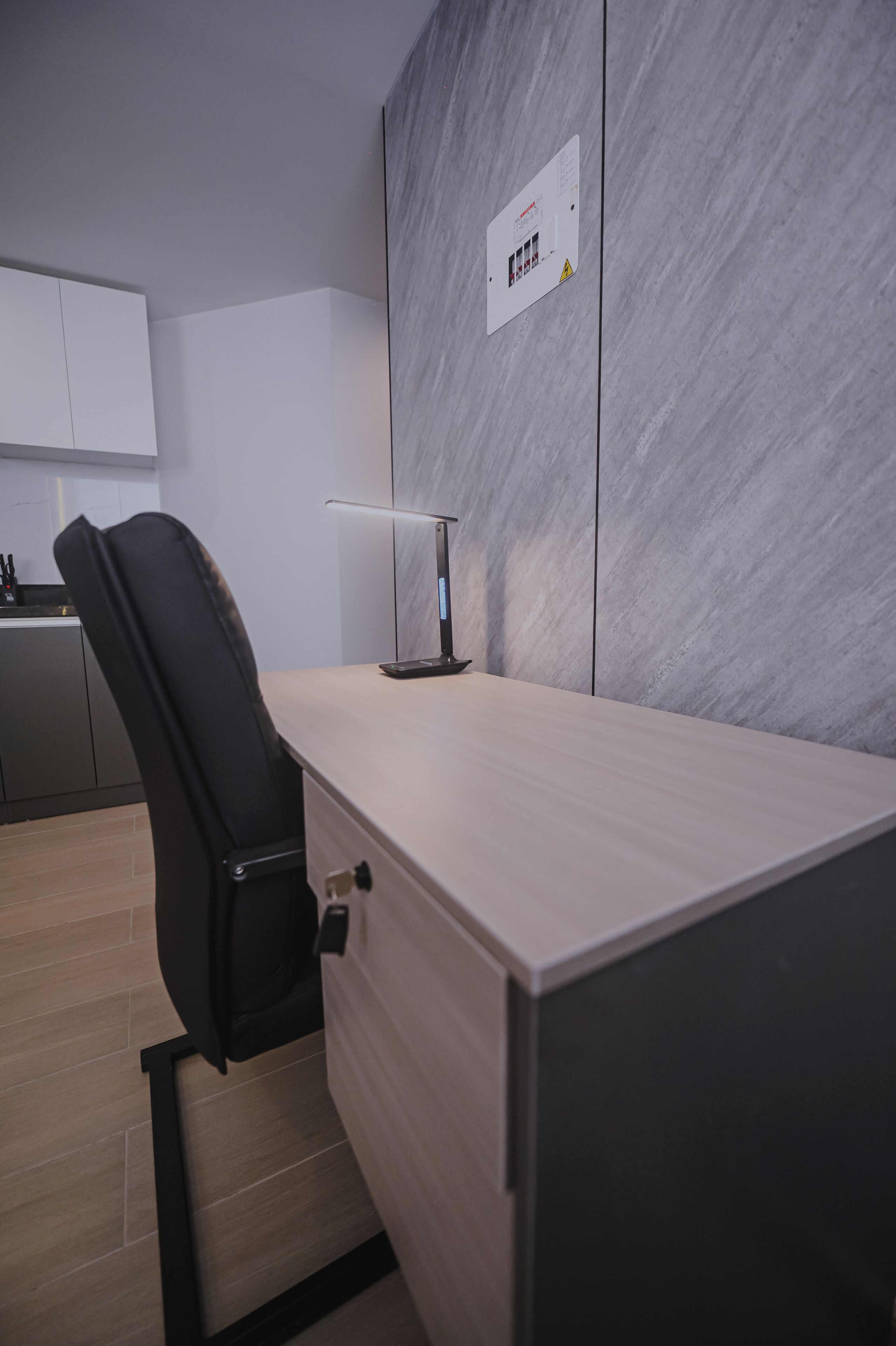 A modern office space with a desk, chair, and a wall-mounted control panel.