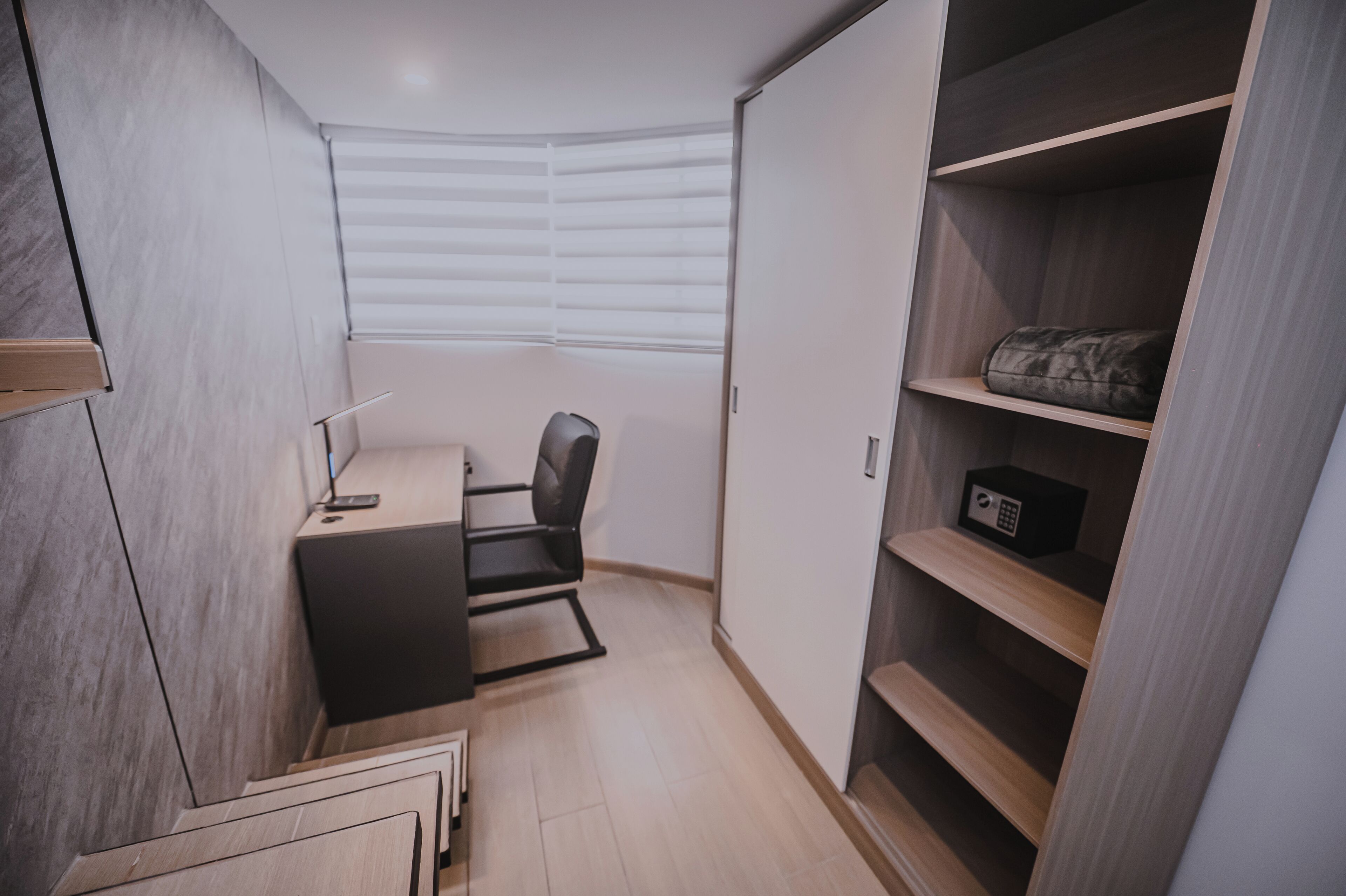 A compact bedroom with a desk, chair, and built-in wardrobe.