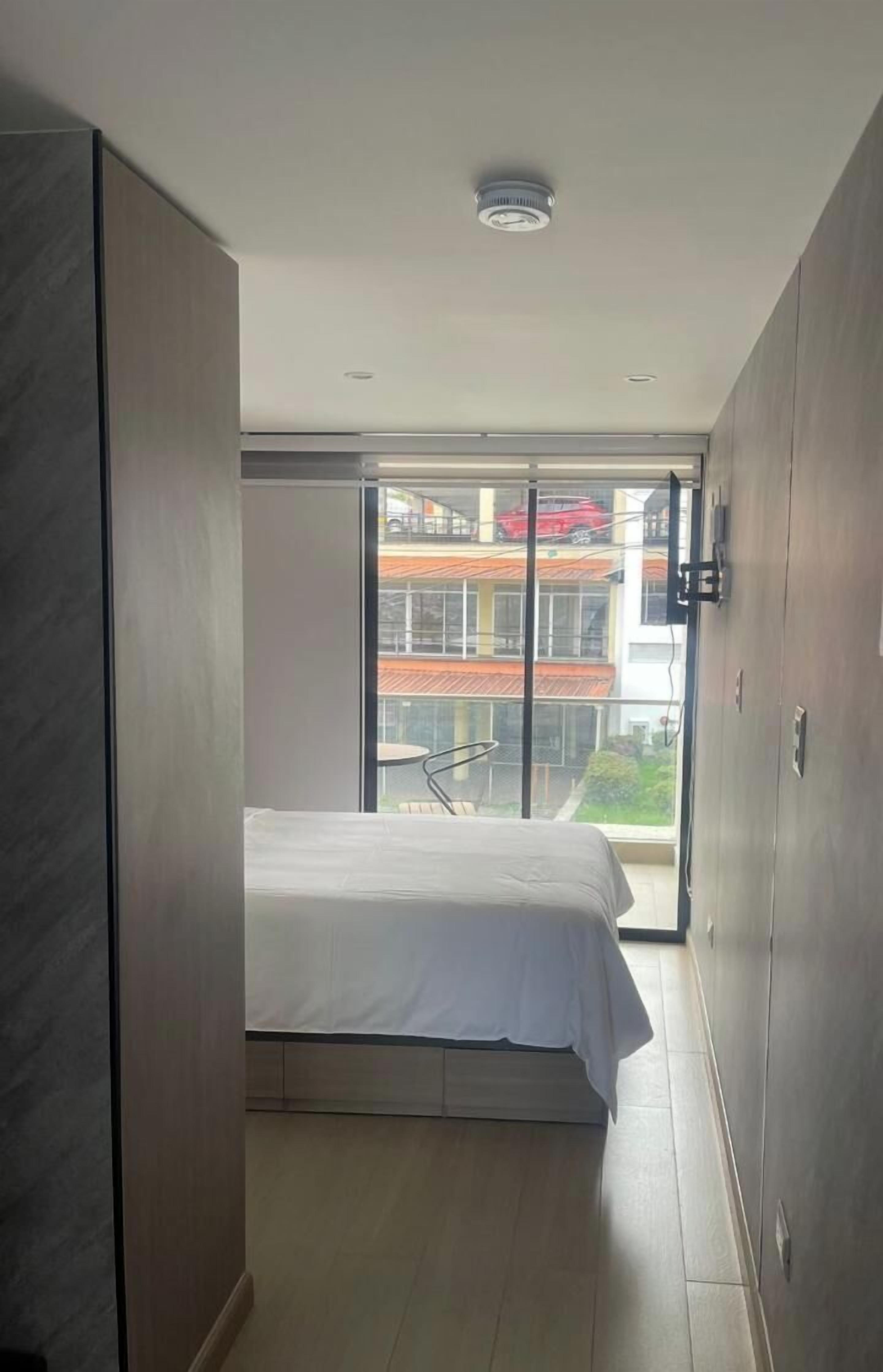 Ein Schlafzimmer mit einem Bett, einer Schiebetür, die auf einen Balkon führt, und einer Deckenleuchte.