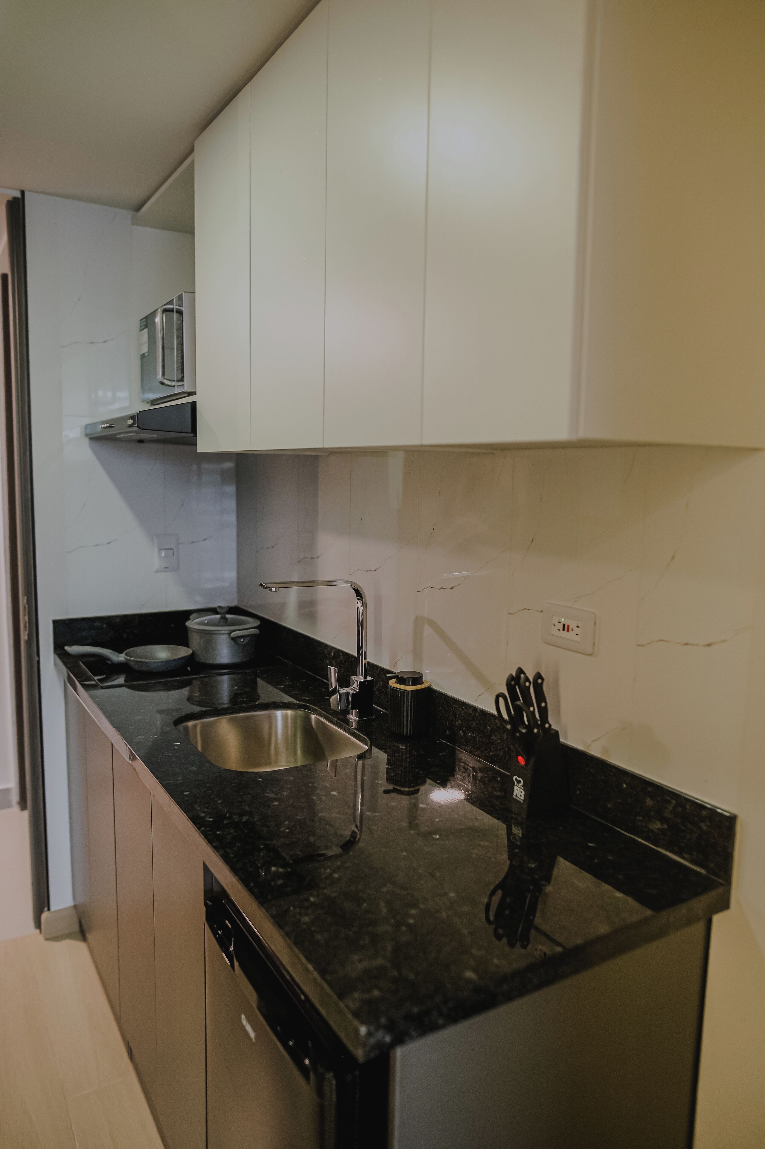 Een moderne keuken met witte kasten, een zwart aanrecht, een roestvrijstalen spoelbak en een vaatwasser.