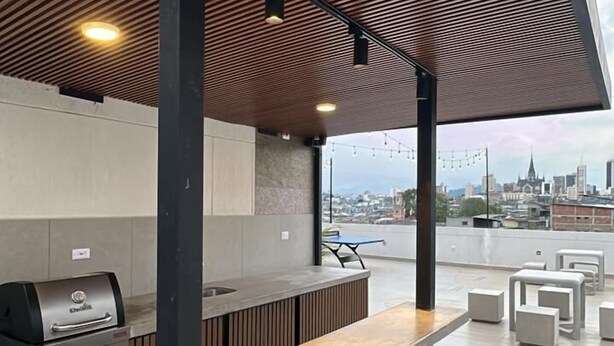 An outdoor bar area with a grill, seating, and a view of the city skyline. - Torre U Kooliving (Manizales)