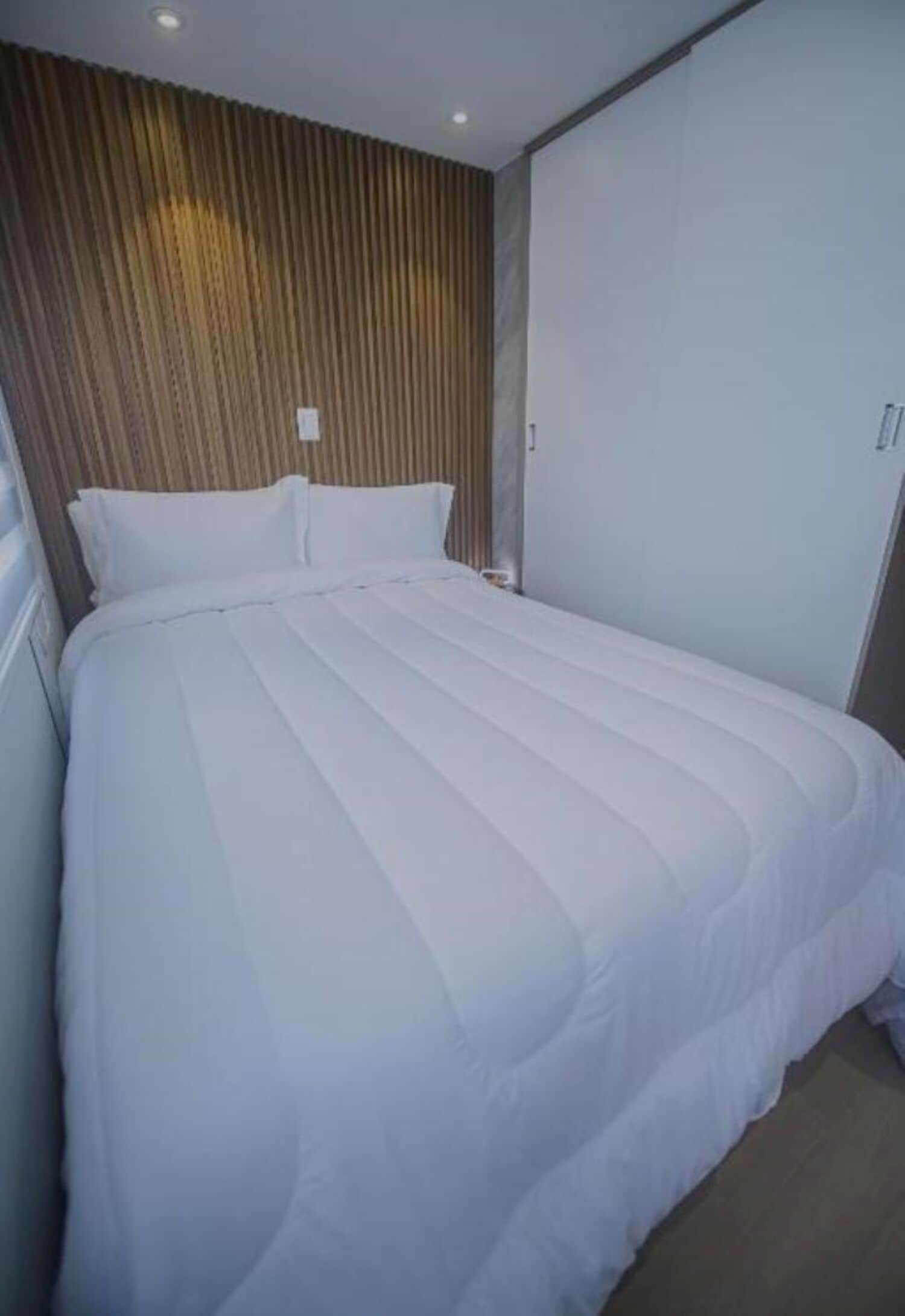 A neatly made bed with white bedding in a room with a wooden slatted headboard and a plain wall.