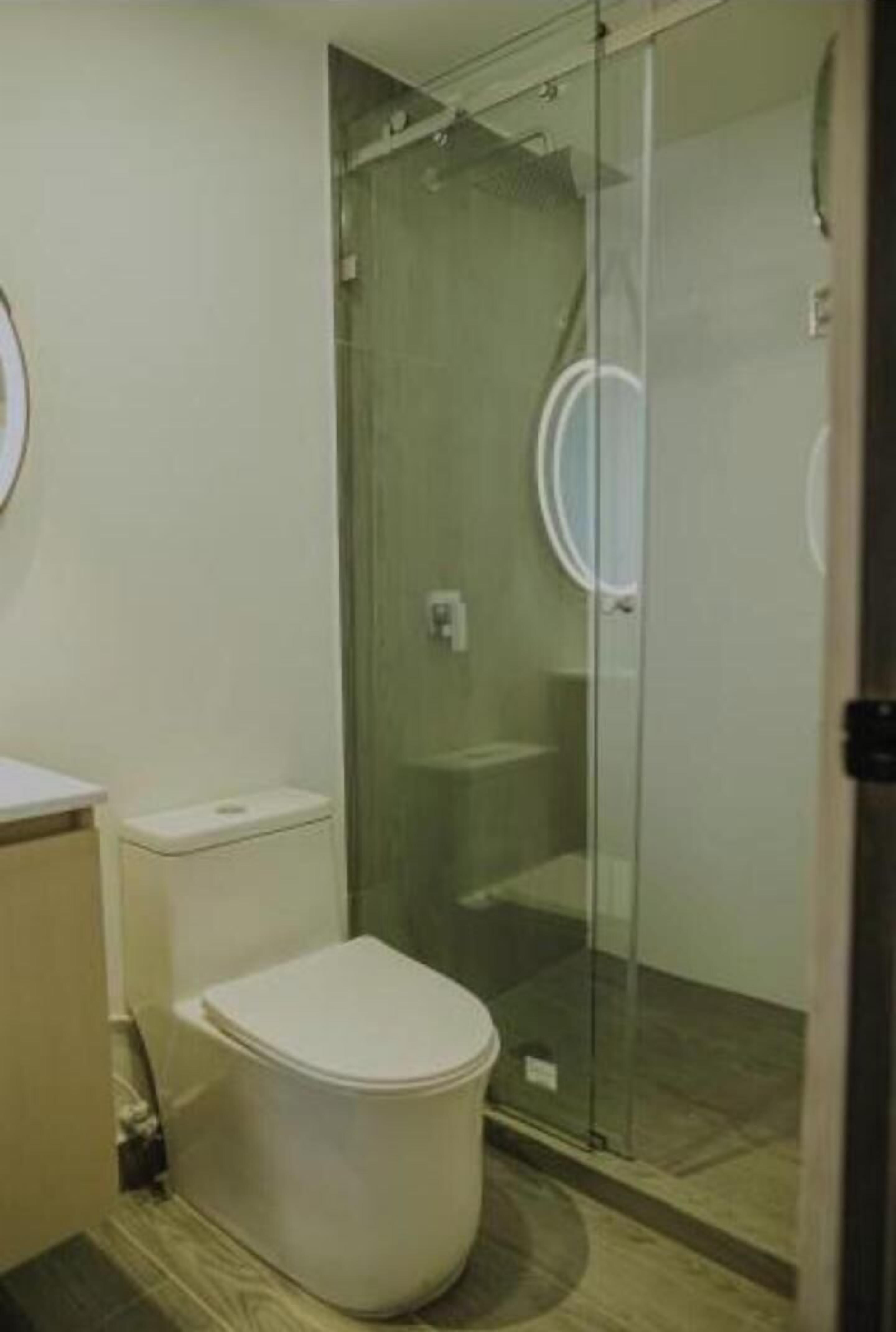 Un baño con inodoro, ducha con mampara de vidrio y lavamanos.