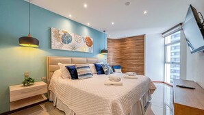 Quarto moderno com uma cama grande, uma mesa de cabeceira, televisão na parede e uma janela com vista para a cidade.