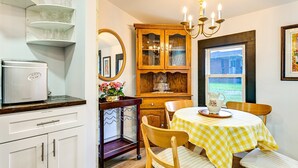 A kitchen with a modern appliance, a wooden cabinet with glass doors, a dining table with a checkered tablecloth, and a chandelier. - Downtown Cornelius Bungalow  Walk to Dining & Cain Center Karaoke + Darts (Cornelius)