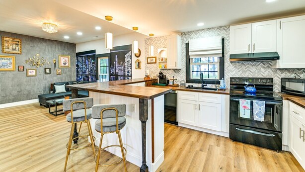 A modern kitchen with a central island, bar stools, a built-in oven, and a herringbone-patterned backsplash. - Downtown Cornelius Bungalow  Walk to Dining & Cain Center Karaoke + Darts (Cornelius)
