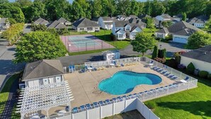 Un quartier résidentiel doté d’une piscine entourée d’une clôture, d’un court de tennis et de maisons en arrière-plan.