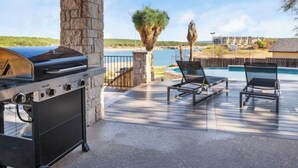 An outdoor patio with a grill, lounge chairs, and a view of a body of water and distant buildings.