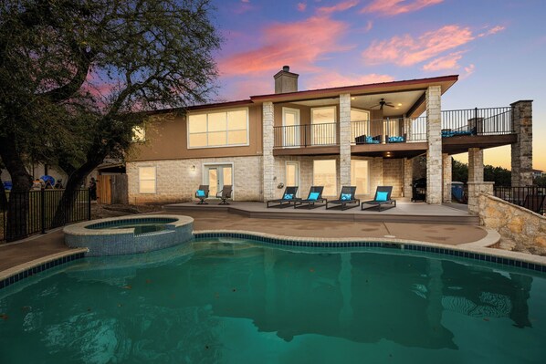 A two-story house with a swimming pool, outdoor seating, and a stone facade.