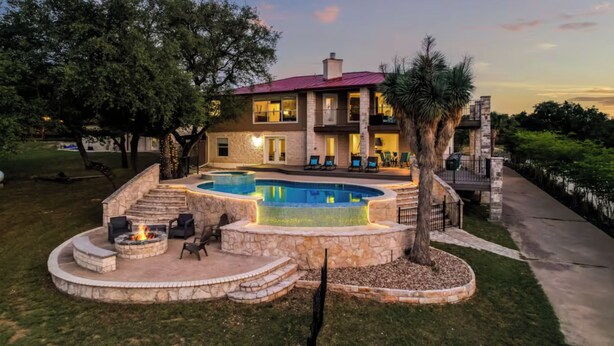 A two-story house with a swimming pool, stone fire pit, and outdoor seating.