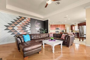 A modern living room with a brown leather sectional sofa, a white coffee table, and a kitchen in the background.