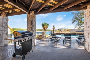 Un espace extérieur abrité, doté d’un barbecue, de chaises longues et offrant une vue sur une piscine et des bâtiments situés au loin.