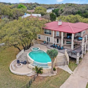 Une maison à deux étages avec un toit rouge, une piscine et un patio aménagé avec du mobilier d’extérieur.