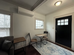 A room with a wooden table, two chairs, a window, a door, and a patterned rug.