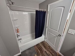 Ein Badezimmer mit einer weißen Badewanne, einer Duschvorhang, einem Handtuchhalter und einer Tür.