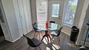 A dining area with a glass table, four chairs, and a red vase. There are white cabinets and a trash bin. - Shagbark - 7 Beds - 4 Baths (St. Peters)