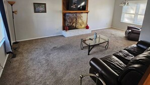 A living room with a fireplace, a leather couch, a glass coffee table, and a TV on a wooden shelf. - Shagbark - 7 Beds - 4 Baths (St. Peters)