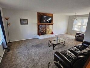 A living room with a fireplace, a leather couch, a glass coffee table, and a TV on a wooden shelf. - Shagbark - 7 Beds - 4 Baths (St. Peters)