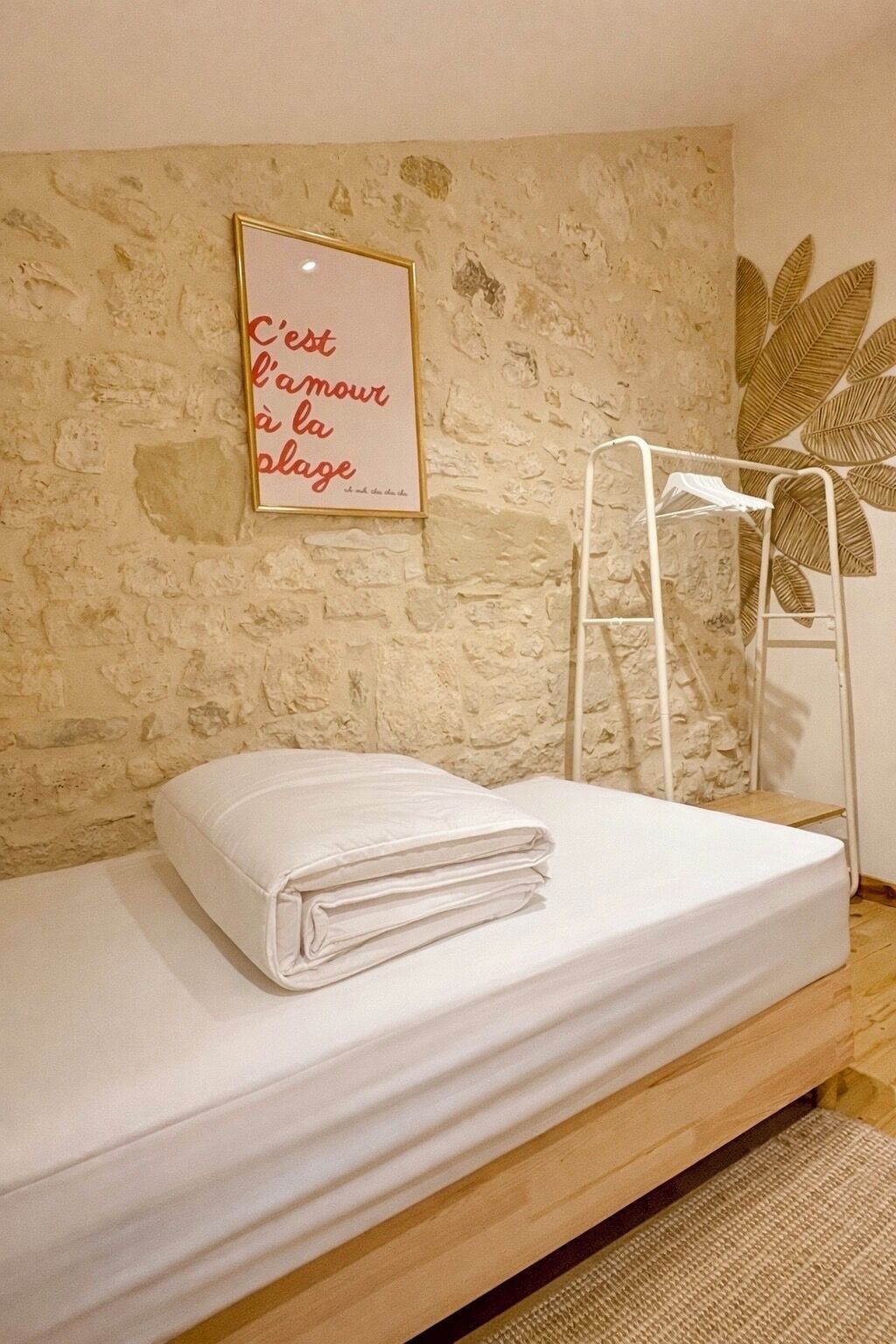 A single bed with a white mattress and a folded white pillow, a white metal ladder, and a wall with a textured stone pattern.